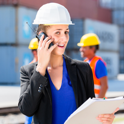 Woman in businesses attire wearing a hard hat holding a walkie talkie